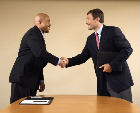 Two businessmen in suits shaking hands and smiling.